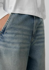 Svijetloplavi traperici s izblijedjelim završetkom, prikazuju ravni kroj, vidljivo šivanje i strgane rubove. Upareni s bijelom košuljom.