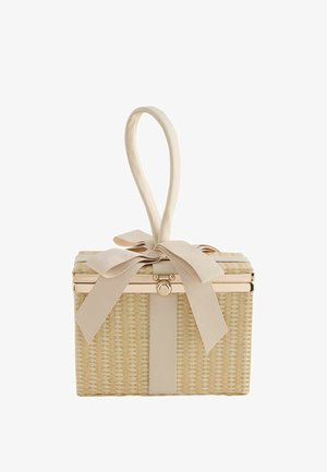 Cesta rectangular de mimbre con asa de tela beige formada en un lazo, sujeta por una gran cinta beige anudada en forma de lazo sobre fondo blanco.