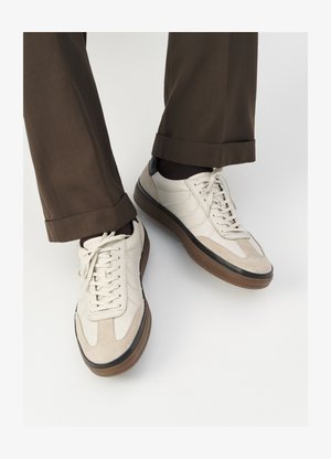 Beige sneakers med en struktureret ruskind front, glatte lædersider og en brun gummisål. Snørebånd og let stikning er inkluderet.
