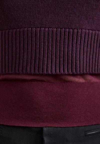 Pull bourgogne avec un col et un ourlet nervurés texturés. Matière douce avec une finition lisse, superposé à un vêtement de couleur plus claire.