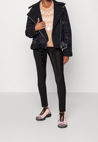 Chaqueta de shearling negra, suéter beige con estampado, leggings negros brillantes y zapatillas con detalles plateados y acentos rosas.