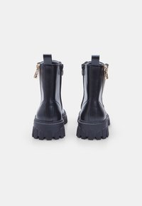 Botas de cuero negro hasta el tobillo con una suela gruesa. Presenta un zipper lateral, una tira para tirar y costuras visibles en el eje. Suela de goma texturizada.