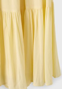 Close-up of a light yellow, tiered dress with gathered seams and a crinkled fabric texture, hanging freely against a plain background.