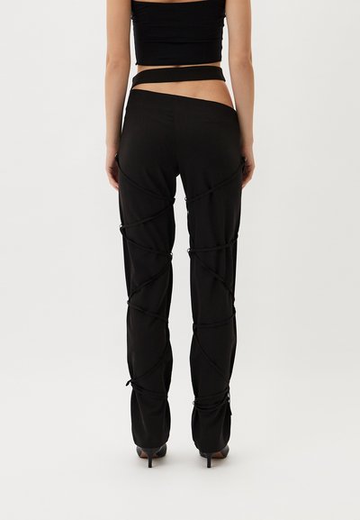 Black pants with ruched detailing and decorative ties, made from a smooth fabric, featuring a fitted design and tapered legs.