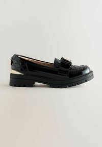 Schwarze Lackleder Slipper mit einer klobigen schwarzen Sohle, dekorativem Schnallendetail und strukturierten Akzenten im oberen Bereich für zusätzlichen Stil.