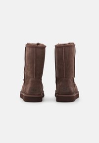 Bruine suede laarzen tot halverwege het kalf met een zachte voering, stikdetails en een platte rubberen zool. Voorzien van een logo-patch op de achterkant.