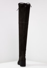 Bota de ante negra hasta la rodilla con punta redonda, tacón grueso y un detalle de lazo en la parte superior. Material texturizado con detalles de costura vertical.