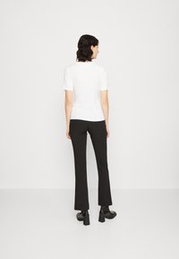 Tricou alb cu mânecă scurtă, asociat cu pantaloni negri evazați, ambele realizate dintr-un material neted. Tricoul are un gât rotund; pantalonii sunt ajustați.