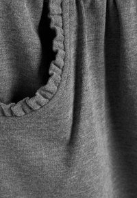 Un tissu gris au toucher doux présente un détail de volants froncés autour de la zone du cou, mettant en valeur un design décontracté.