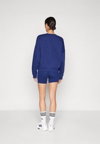 Felpa oversize blu navy con spalle scese, abbinata a pantaloni corto fitted coordinati. Calzini bianchi con strisce nere e scarpe sportive.