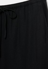 Pantalon en tissu noir avec une taille élastique et un cordon à nouer à l'avant, présenté sur un fond blanc.