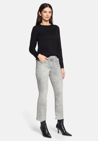 Czarny sweter z długim rękawem w połączeniu z jasnoszarymi dżinsami z postrzępionym dołem i dekoracyjnymi detalami, dopełniony czarnymi botkami na obcasie.