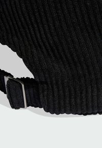 Čierna kordová tkanina so zvislými ryhami, s kovovou prackou a remienkom pre nastaviteľné upevnenie, prezentujúca textúrovaný povrch.