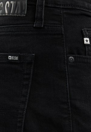 Schwarze Jeans aus Denim mit sichtbaren Gesäßtaschen, Gürtelschlaufen und kleinen "BIG STAR" Markenetiketten in der Nähe der Taschen.