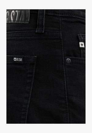 Mustad teksapüksid nähtavate tagataskute, vööaasade ja taskute lähedal väikeste "BIG STAR" kaubamärgi siltidega.