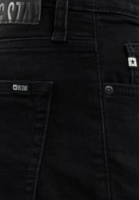 Fekete farmernadrág látható hátsó zsebekkel, övbújtatóval és kis "BIG STAR" márkajelzésű címkékkel a zsebek közelében.