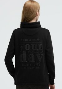 Black hooded sweatshirt with a soft texture, featuring embossed text on the back: "your day Adventure CABIN LIFE SOCcx SPIRIT."