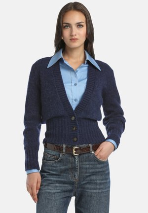 Navy blue cropped cardigan with ribbed texture, featuring a V-neck, button closure, and long sleeves. Paired with a light blue shirt and denim jeans.