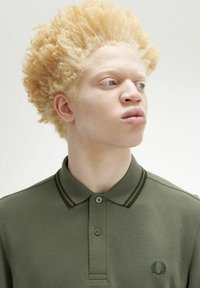 Polo shirt verde oliva con materiale testurizzato, pattina a due bottoni e strisce scure a contrasto sul colletto. Caratterizzato da logo ricamato.