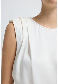 Hvid ærmeløs top med plisserede skulderdetaljer, glat tekstur, rund halsudskæring og blødt stof skaber et minimalistisk design.