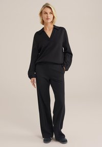 Melnā garām piedurknēm tops ar V-veida kakla izgriezumu un apkakli, kombinēts ar plašām melnām biksēm. Gluda auduma, bez rakstiem, vienkārša dizaina.