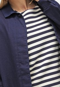 Giacca camicia blu navy sopra una maglietta a righe crema e blu navy; presenta un colletto e tessuto testurizzato.