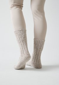 Calcetines de punto beige con una textura acanalada, que se extienden por encima del tobillo, mostrando un color claro y un material suave y acogedor.