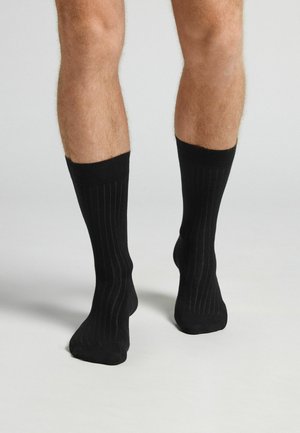 Medias negras hasta la rodilla con textura acanalada vertical. Material suave y parte superior elástica, que se ajusta perfectamente alrededor de las pantorrillas.