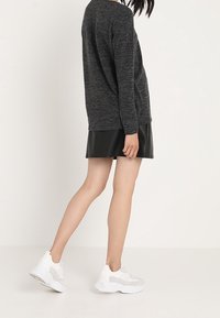 Haut en maille grise à manches longues associé à une mini-jupe en cuir noire et des baskets blanches de sport, affichant un style décontracté moderne.