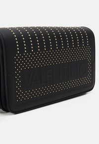 Borsa a mano nera in pelle con borchie dorate disposte in modelli verticali e orizzontali. Presenta un logo impresso sul fronte.