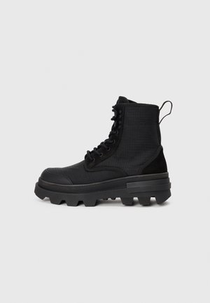 Botas de tobillo negras con parte superior de tela texturizada, suela de goma y tacos prominentes. Las características incluyen ojales reforzados y una lengüeta.