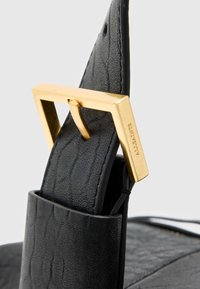 Zwart gestructureerd leren tasriem met een gouden rechthoekige gesp en een lus. Het materiaal heeft een subtiel patroon en een gladde afwerking.