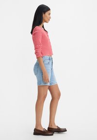 Röd och vit randig långärmad tröja, ljusblå jeansshorts, bruna loafers. Sidoprofil med slät textur och avslappnad passform.