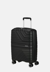 Valigia rigida nera con una finitura testurizzata, dotata di manico telescopico, quattro ruote e chiusura a zip. Testo che recita "American Tourister".