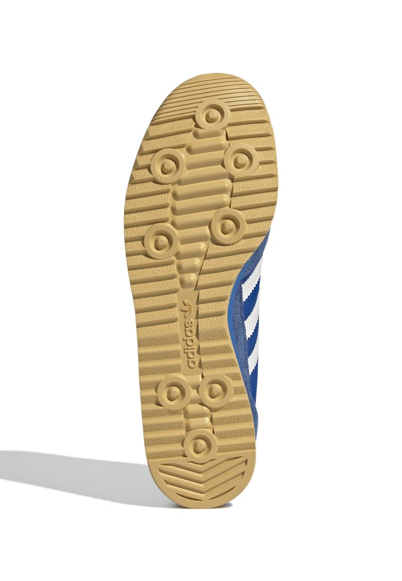 Semelle de chaussure de sport bleue avec une semelle extérieure en caoutchouc gomme texturé présentant des motifs de grip circulaires et horizontaux. Rayures blanches sur le côté.