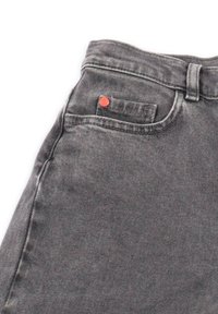 Jeans in denim grigio con una piccola tasca frontale per monete caratterizzata da un rivetto rosso, che mostra i dettagli della vita e dei passanti per cintura.