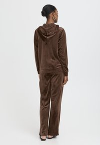 Survêtement en velours marron avec un haut à capuche et un pantalon assorti. Texture lisse, coupe décontractée et léger éclat dans le tissu.