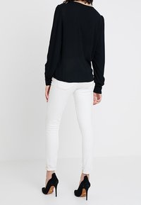 Blusa nera a maniche lunghe con spalle arricciate, abbinata a jeans skinny bianchi e scarpe con tacco nere. Design semplice e aderente.