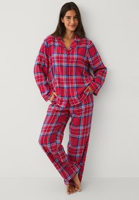 Rødt ternet flannel pyjamasæt med knaplukket bluse med lange ærmer og matchende bukser, begge i et ternet mønster med blå accenter.