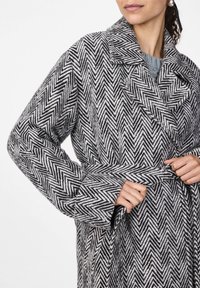 Cappotto in lana bicolore a spina di pesce con ampi risvolti e design avvolgente, dotato di cintura e tessuto testa di moro.