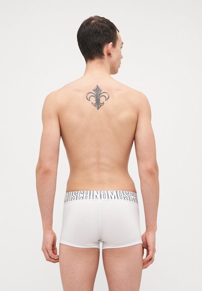White men’s boxer briefs made of soft fabric, featuring a black logo waistband. The back shows a decorative tattoo and a smooth silhouette.