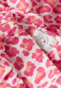 Tissu à imprimé léopard rose et orange, avec des bords froncés et une fermeture à bouton blanc. Texture douce avec des détails de couture visibles.