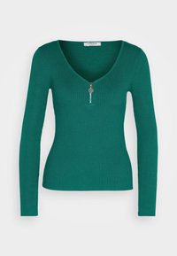 Haut à manches longues côtelé de couleur vert foncé avec un col en V et un détail de fermeture éclair argentée à l'avant. Coupe ajustée, texture lisse et tissu extensible.