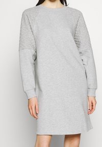 Robe gris clair en tissu doux, avec des accents matelassés sur les épaules et des manches longues, au fit décontracté et aux poignets côtelés.