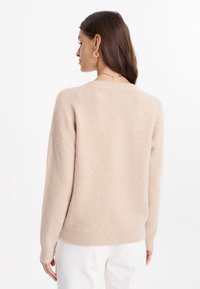 Maglione beige realizzato in morbido tessuto a maglia, caratterizzato da una vestibilità ampia, spalle cadenti e orlo e polsini a coste. Texture liscia, design casual.
