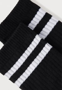 Black socks with ribbed texture, featuring two white horizontal stripes on the upper part. Soft cotton material with elastic cuff.