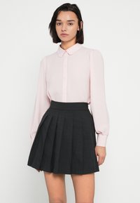 Απαλή ροζ μπλούζα με μακριά μανίκια, γιακά και κουμπιά· συνδυασμένη με φούστα σκούρου γκρι με πιέτες και ψηλή μέση.