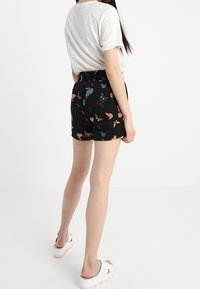 Svarta shorts med en fjärilsprint i olika färger. Midjan är elastisk. Tillsammans med en ljusgrå t-shirt och vita slip-on skor.