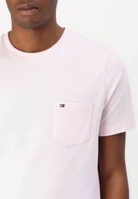 Rosa bomulls t-skjorte med rund hals, korte ermer, og en brystlomme med en liten logo i rødt, hvitt og blått.