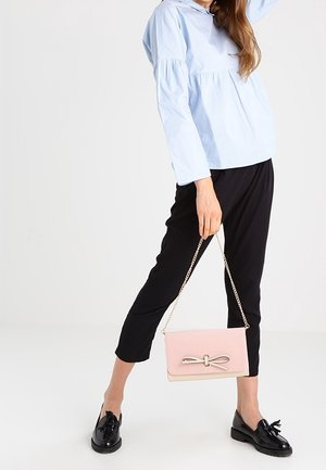 Top peplum azzurro chiaro, pantaloni neri plissettati e una borsa rosa con dettaglio a fiocco, dotata di una tracolla a catena e superficie liscia.